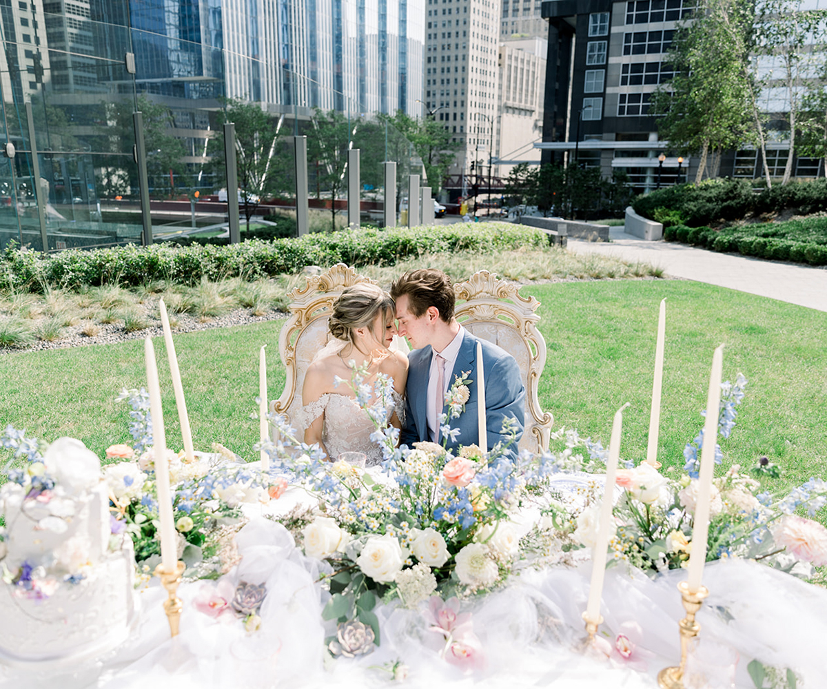 A bride and groom sit at their head table in the outdoor courtyard